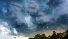 Ilustrasi awan gelap menggantung di langit Jakarta dengan rintik hujan ringan.
(Posnews/Canva)