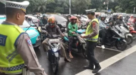 Petugas Satlantas Polres Metro Jakarta Barat membagikan brosur Operasi Keselamatan Jaya 2026 kepada pengendara di persimpangan jalan. (Posnews/Ist)