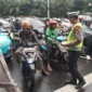 Petugas Satlantas Polres Metro Jakarta Barat membagikan brosur Operasi Keselamatan Jaya 2026 kepada pengendara di persimpangan jalan. (Posnews/Ist)