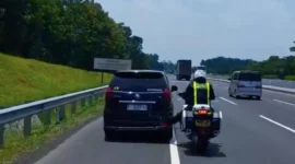 Seorang polisi lalu lintas mendorong mobil mogok dengan kaki di Tol Cikopo–Palimanan (Cipali) saat arus mudik Lebaran 2026 viral di media sosial. (Posnews/Instagram)