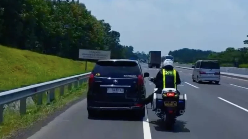 Seorang polisi lalu lintas mendorong mobil mogok dengan kaki di Tol Cikopo–Palimanan (Cipali) saat arus mudik Lebaran 2026 viral di media sosial. (Posnews/Instagram)